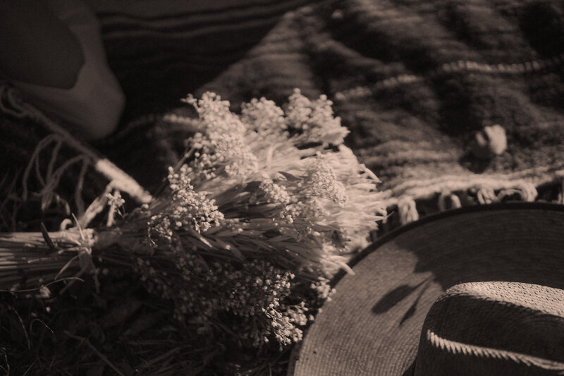 Cowboy hat sits on top of horse blanket next to a bouquet of flowers in the sunlight.