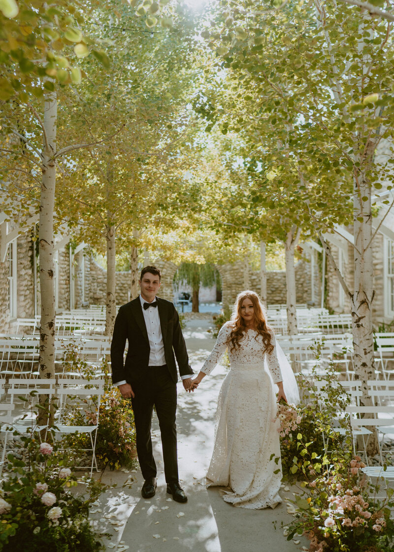 Bride and groom share a kiss in front of a mountain backdrop while  guests throw confetti.