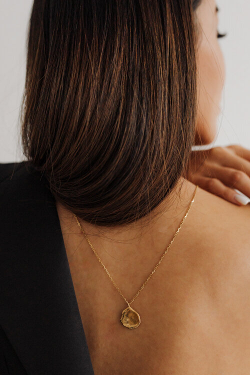 zlatý náhrdelník na zádech ženy s tmavými vlasy