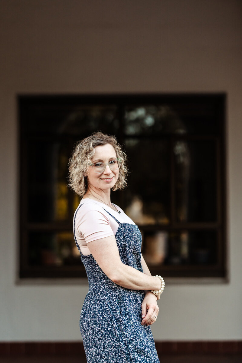 A photographer stands sideways and smiles at the camera for a headshot