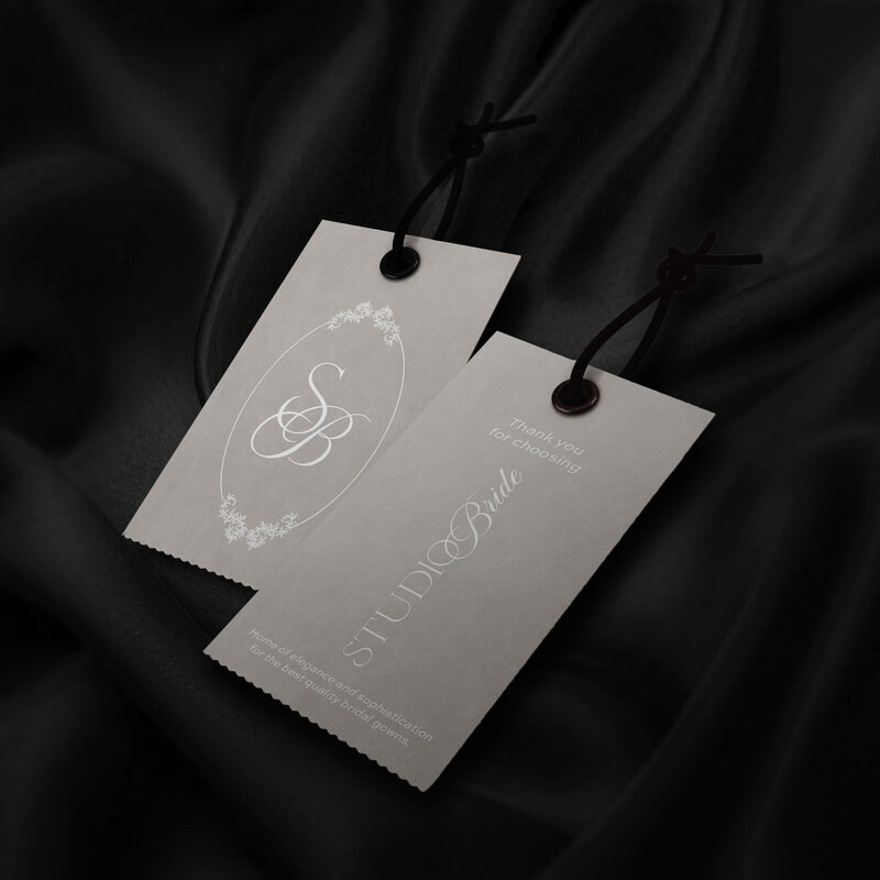 Wedding dress clothing tags that are in the color cream, with the Studio Bride logo, that read, "Thank you for choose Studio Bride, home of elegance and sophistication for the best quality bridal gowns".