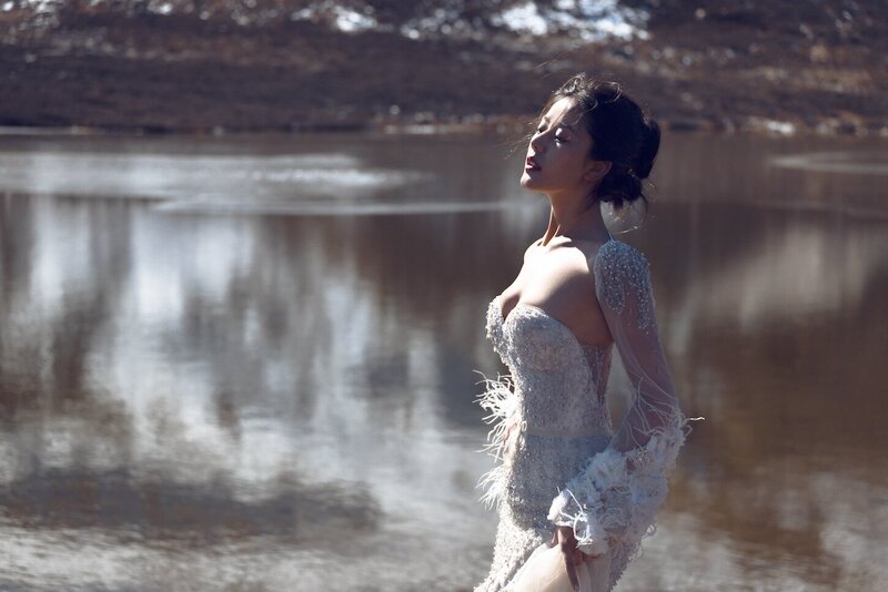 Dramatic shoot of a bride in a haute couture dress by an alpine lake in snow capped mountains.