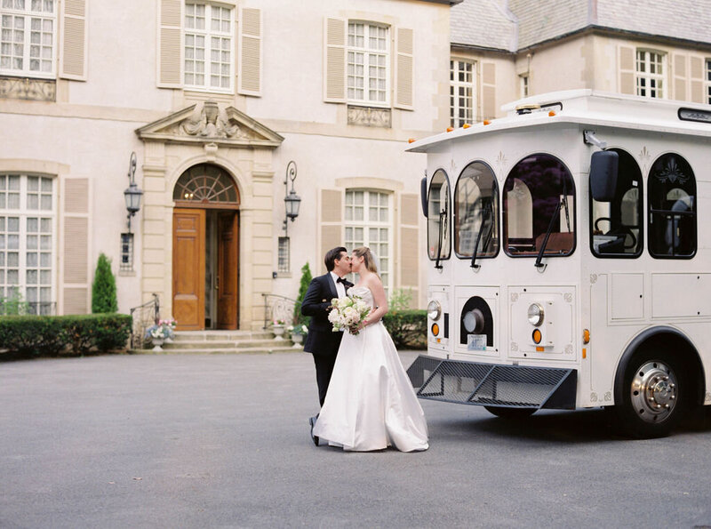 Glen Manor House | A bride and groom share a kiss in front of a white trolley bus, set against an elegant mansion background.