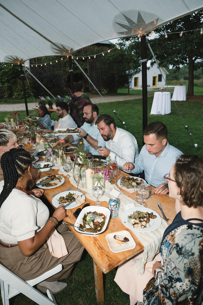 wedding guests eating family style at outdoor farm wedding under a tent