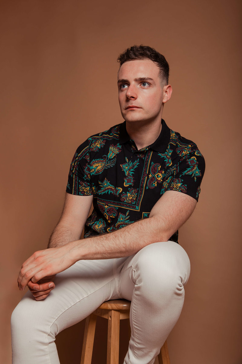 Connor sat cross legged in a studio against a red background, wearing an all-red tracksuit