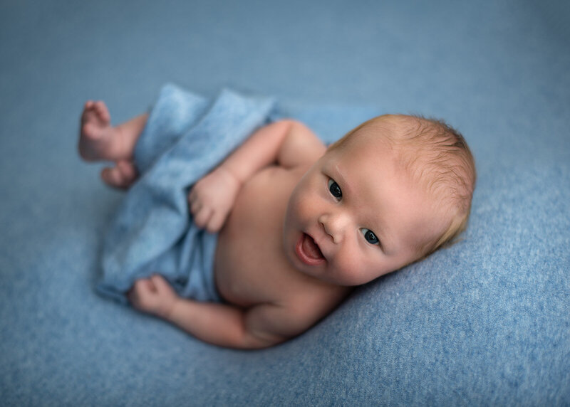 baby on a blue blanket looking at camera and smiling by st. louis newborn photographer, sutherlandphotography
