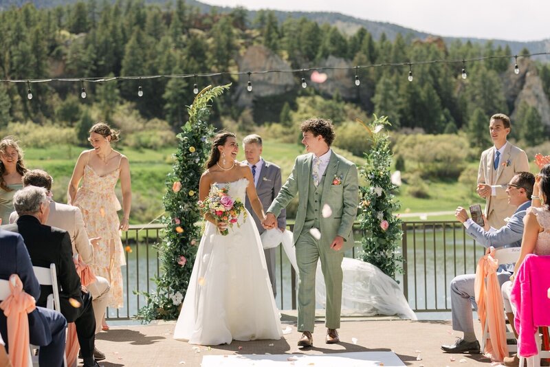 Colorado mountain wedding ceremony exit with joyful bride and groom holding hands as their guests throw rose petals down the aisle.