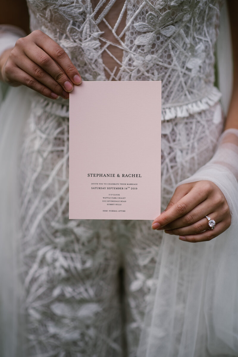 Bride in wedding dress holding pink minimalist elegant wedding invitation