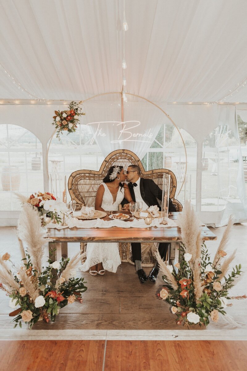 bride and groom kiss at boho sweetheart table