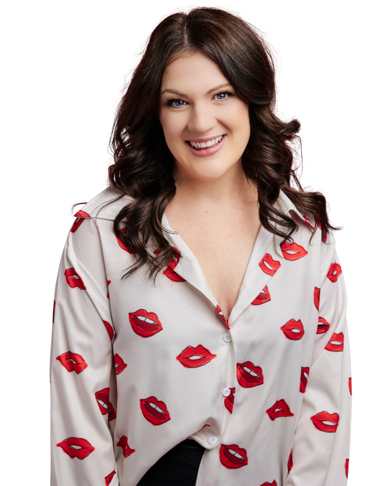 Emily smiling directly at the camera with her hair curled around her shoulders. She is wearing a button up white blouse with red lips pattern all over it.