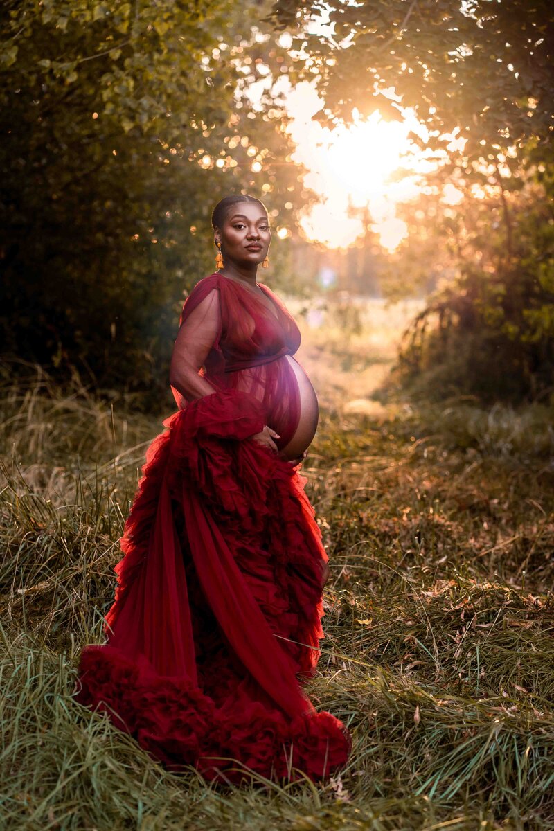 Tacoma maternity photographer documents pregnant mom in sunny forest at sunset wearing a red dress showing her belly.