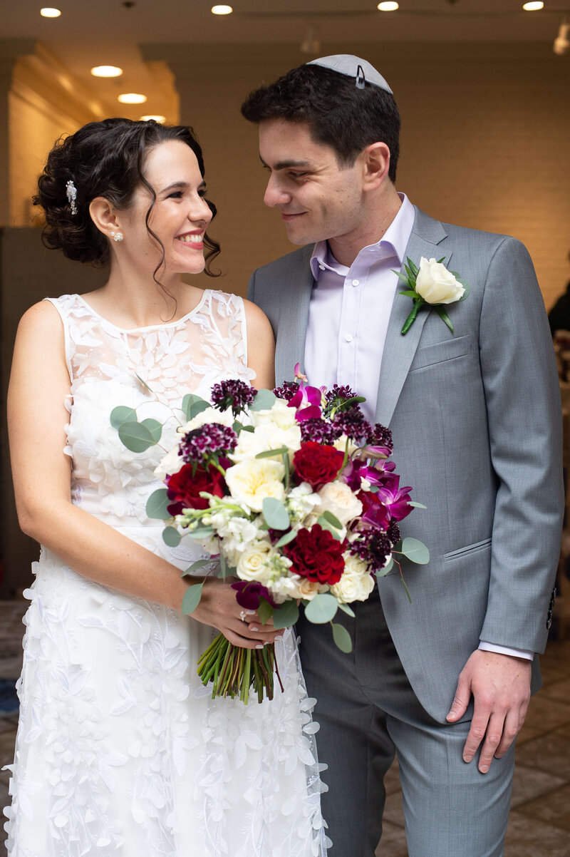 bride and groom smiling at each other with bouquet