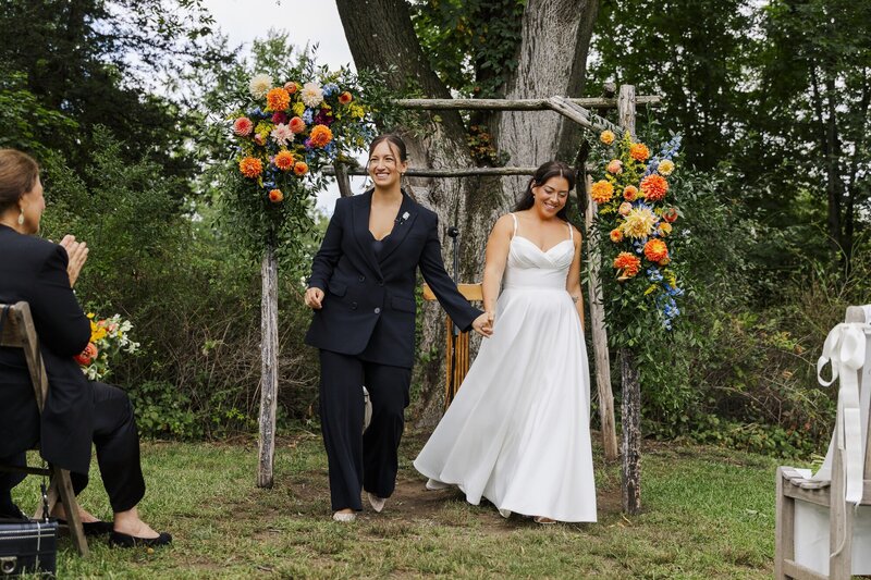 Couple standing together under a floral arch with orange flowers at an outdoor ceremony