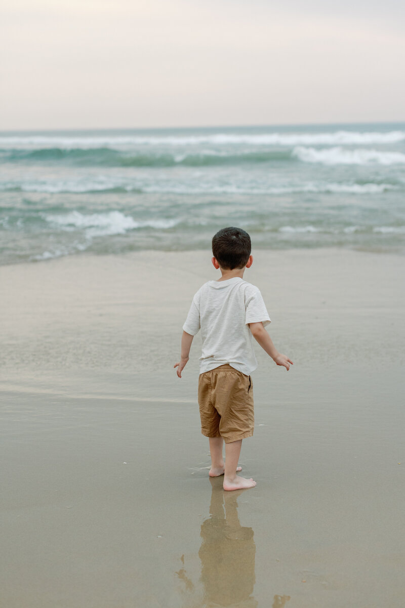 A child stares out at the water during a family beach portrait session