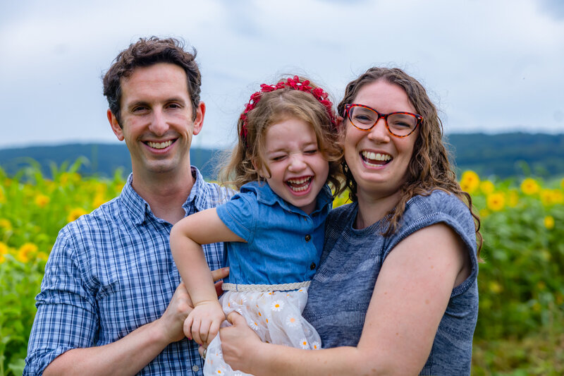 Happy family of three smiling and laughing together during an outdoor photo session in a scenic field – captured by Capture Joy Photography, Northern Virginia family photographer