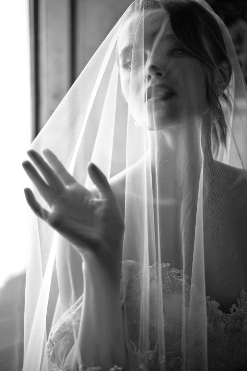 A black-and-white portrait of a bride behind a sheer veil, capturing a romantic and intimate moment by Feyer Photography