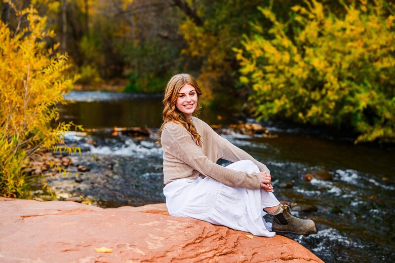 Sedona high school senior sitting by creek fall colors background  crescent moon ranch