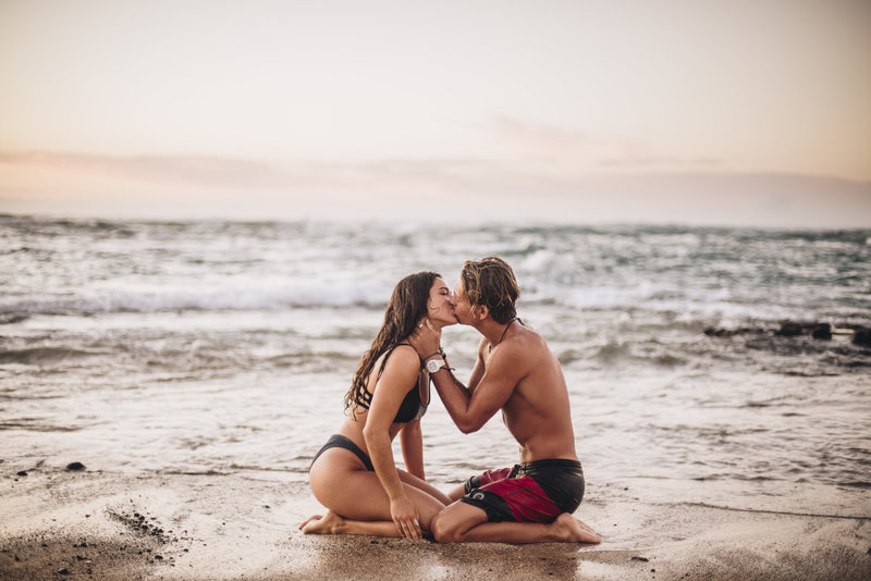 Couple both kneeling on the beach shore kissing each other