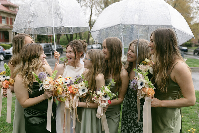 bridesmaids holding pastel flower bouquets and clear umbrellas during a spring wedding in Kansas City, MO
