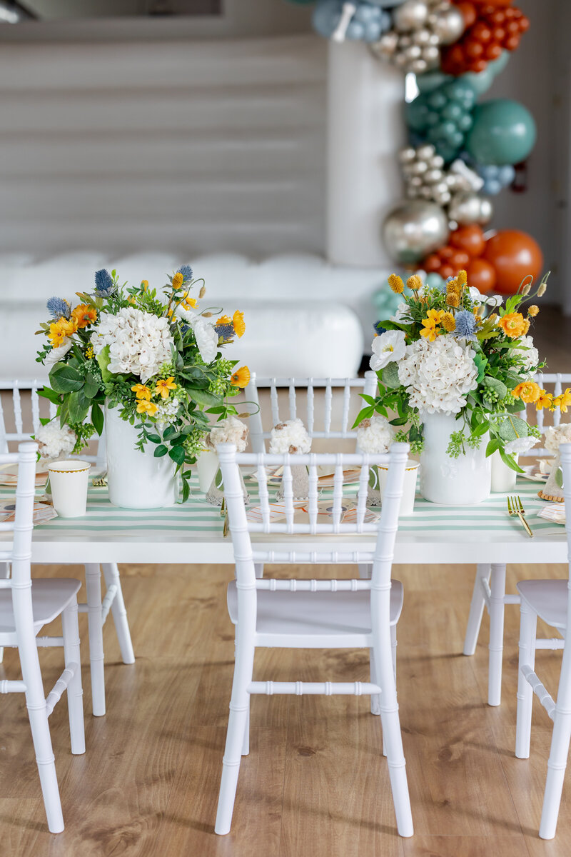 Kids table decorations with white table and chairs, dog treat canisters, flowers and paper goods. 