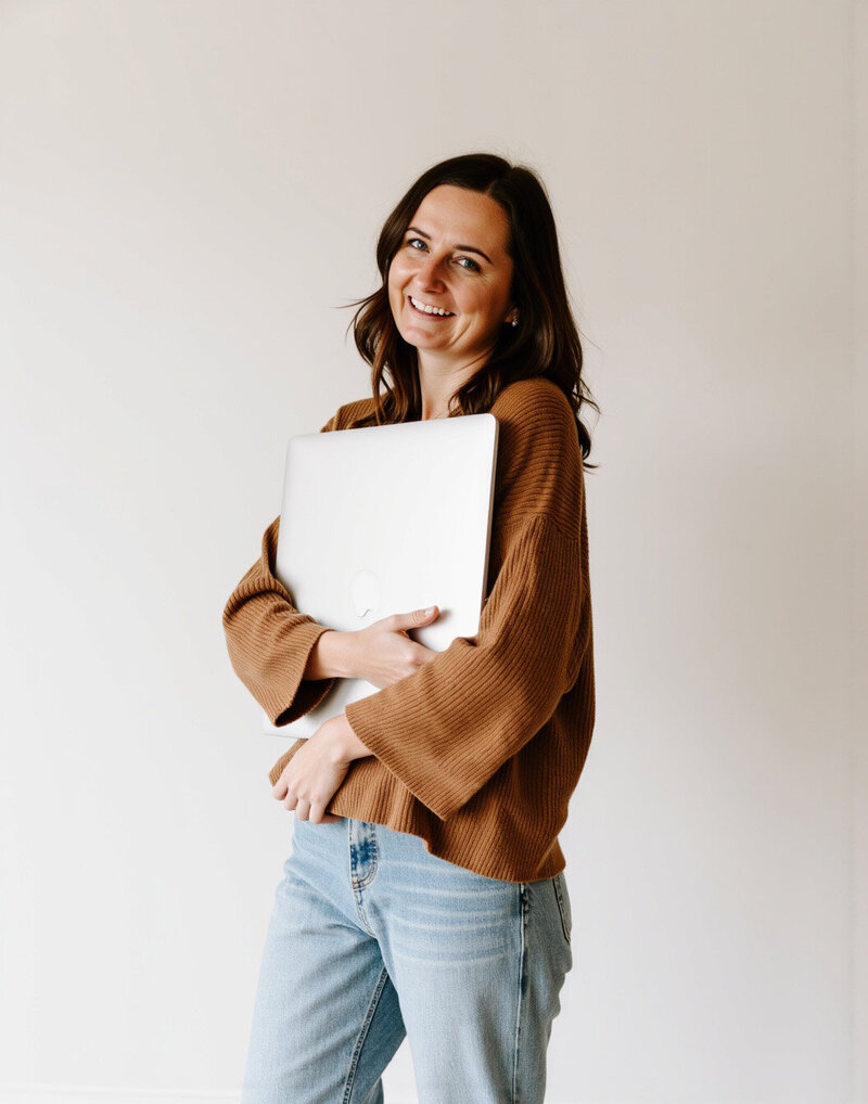 A woman stands in front of a white wall, holding a laptop, showcasing her work as an Ohio website designer.