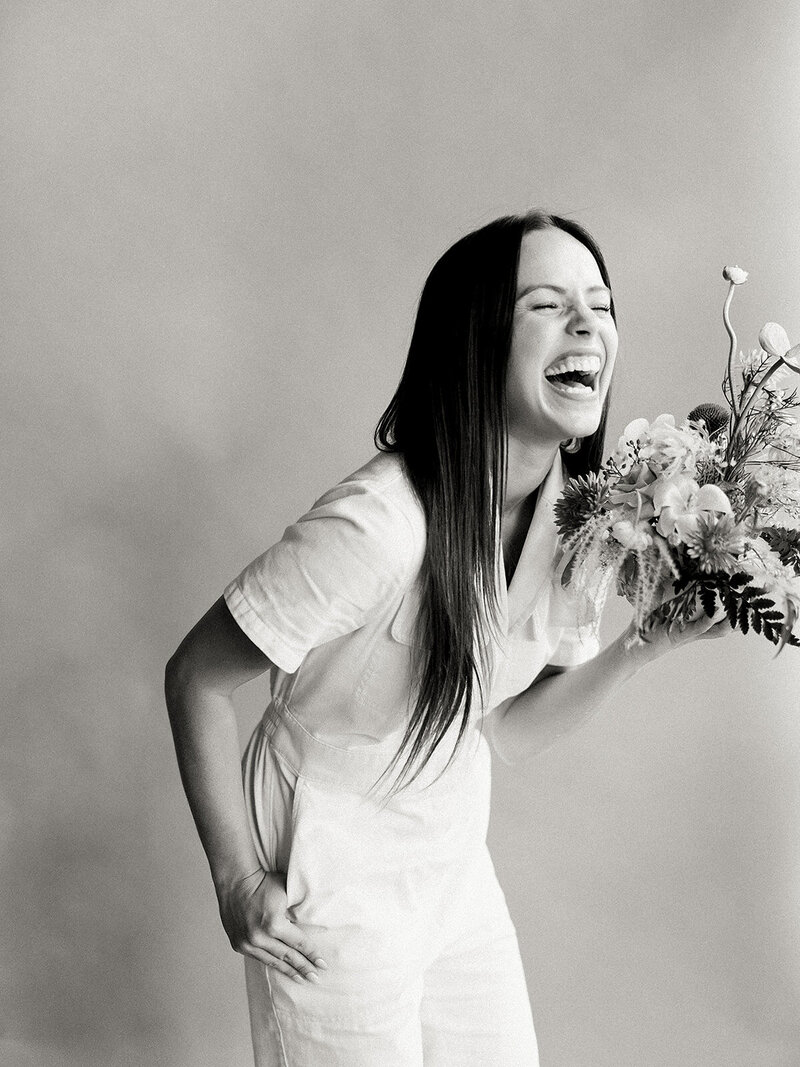 Black and white photo of a girl in a jumpsuit holding flowers and laughing