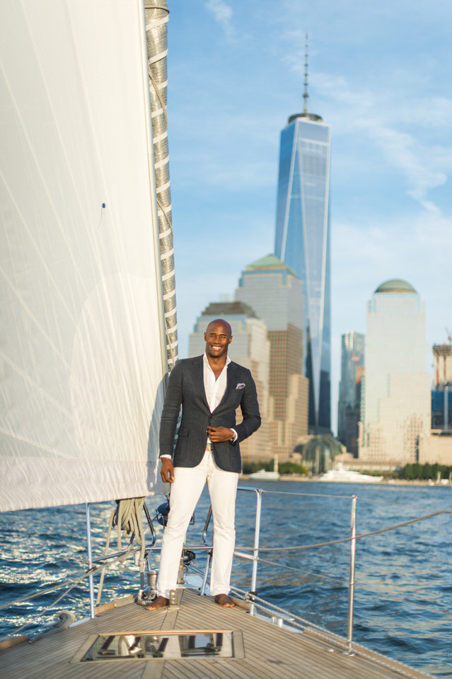 photo of a man on a sailboat with the nyc skyline behind him