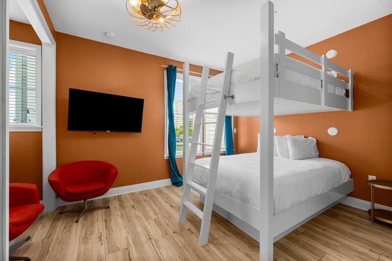Bold orange-walled bedroom with queen-over-queen bunk beds and vintage red chairs at Groovy Shack in Panama City Beach, close to Alys Beach and Santa Rosa.