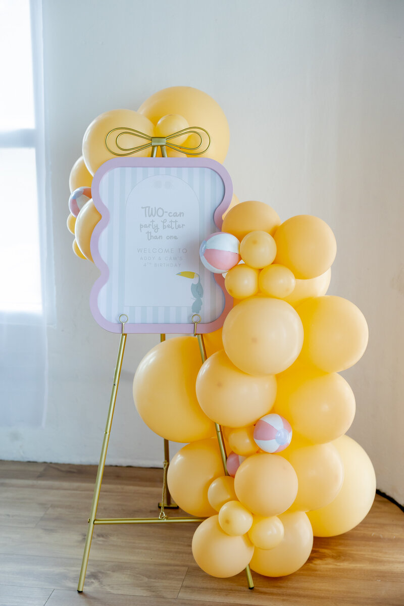 Gold easel with custom sign and yellow balloons and pink small beach balls.