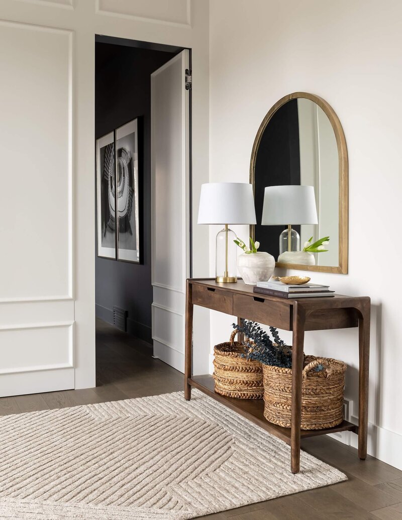 A front foyer with a wood console table, baskets and arched mirror. 