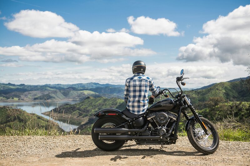 Man sitting on motorcycle sideways looking over water and hills area