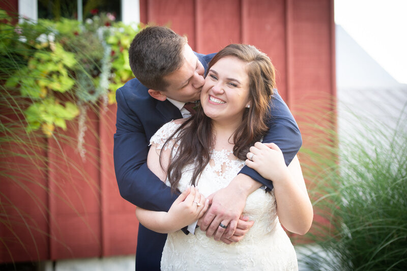 bride smiles at camera while groom kisses her cheek