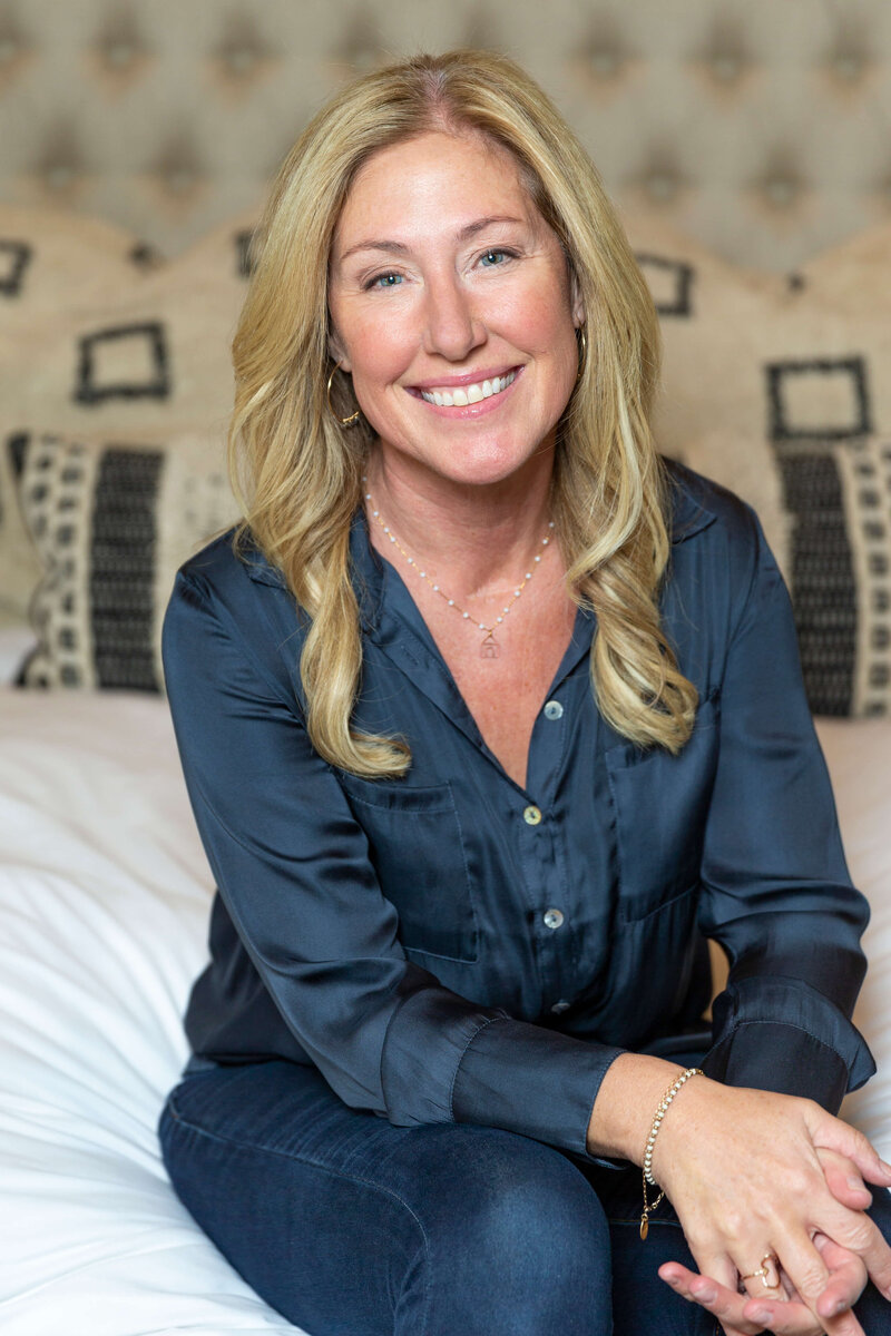 Author Karla Olson sitting on a bed wearing dark blue shirt and pants
