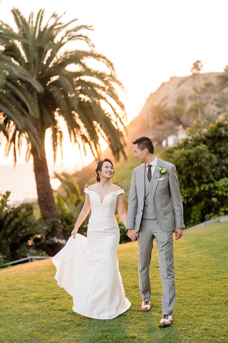 Bride and groom walking hand in hand during golden hour and a big palm tree in the background