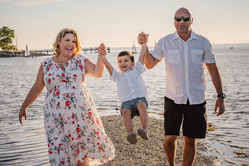 Parents lifting their son up in the air as the sun sets with the ocean behind them.