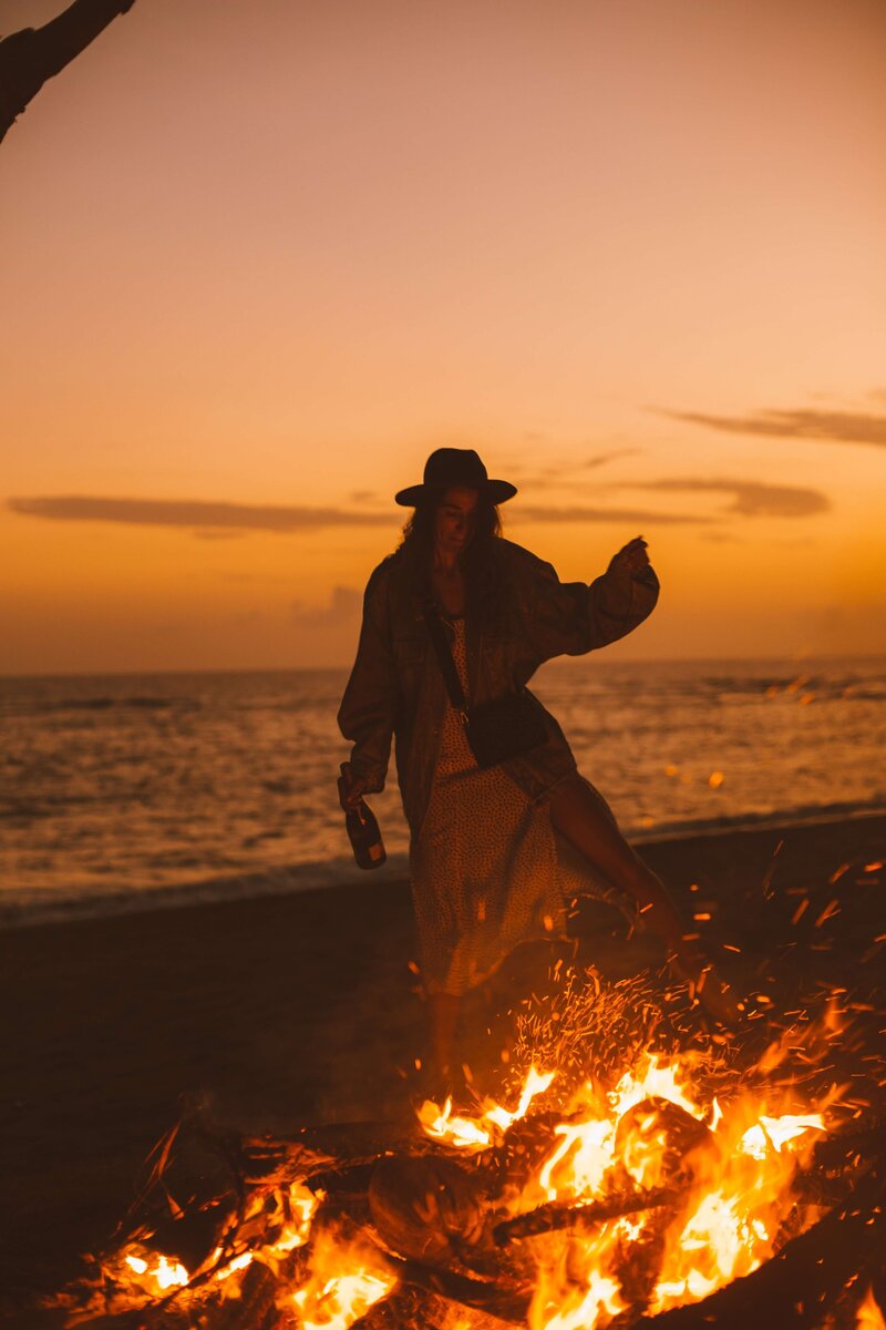 Frau die um ein Lagerfeuer tanz bei Sonnenuntergang