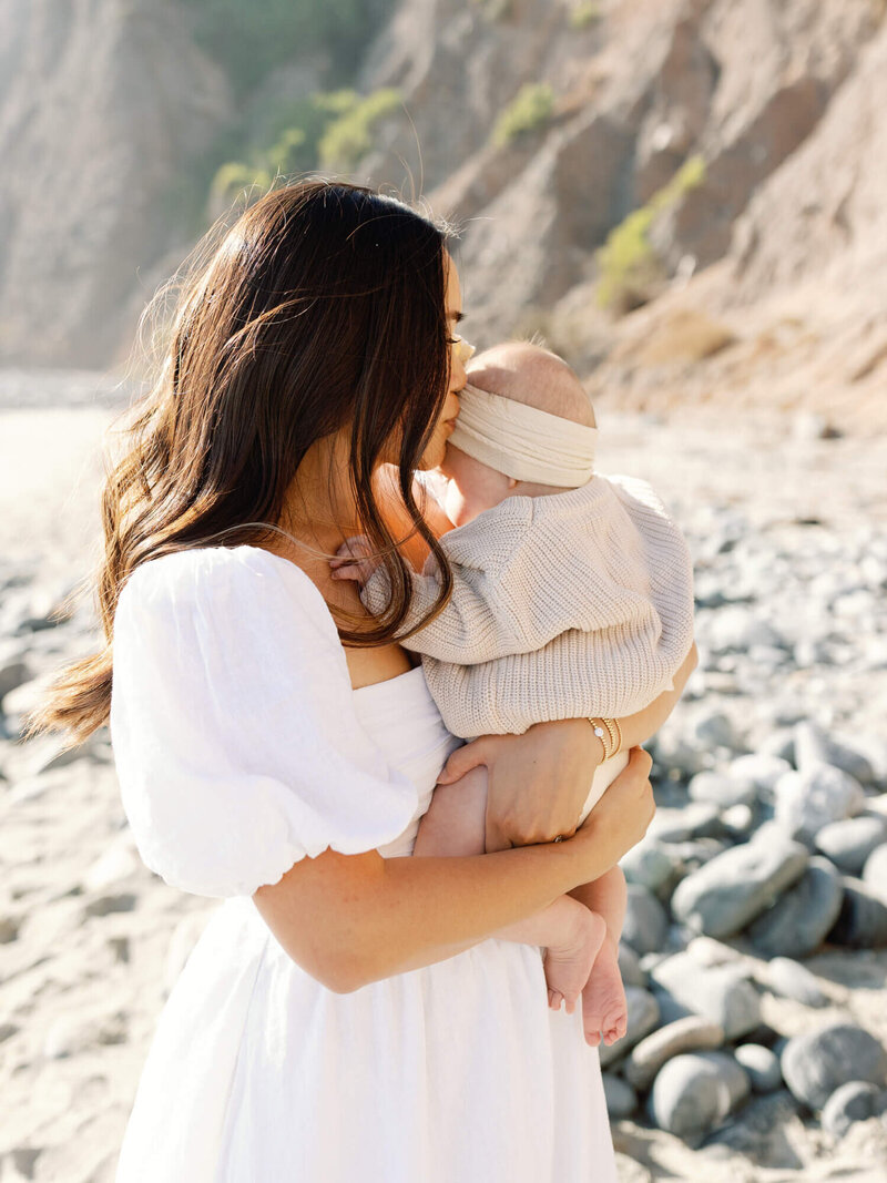 portrait of mom kissing baby at the beach 