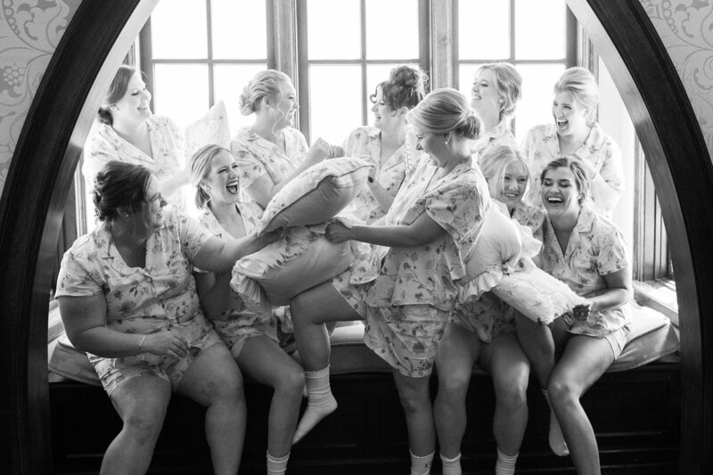 Black and white portrait of bride and bridesmaids having a pillow fight at Dover Hall Estate