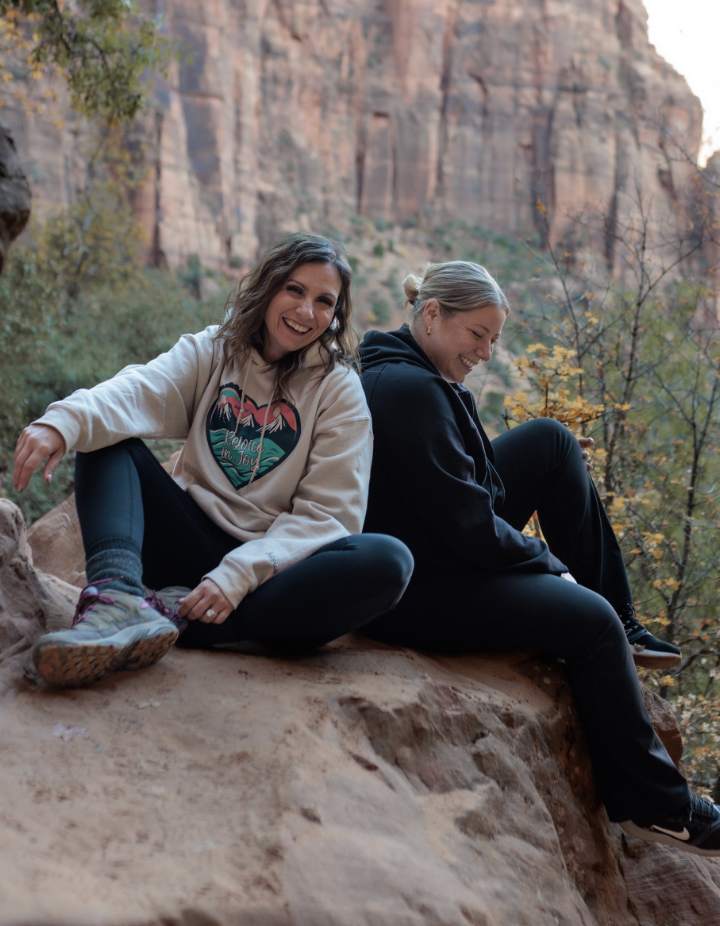 two women sitting on boulder laughing
