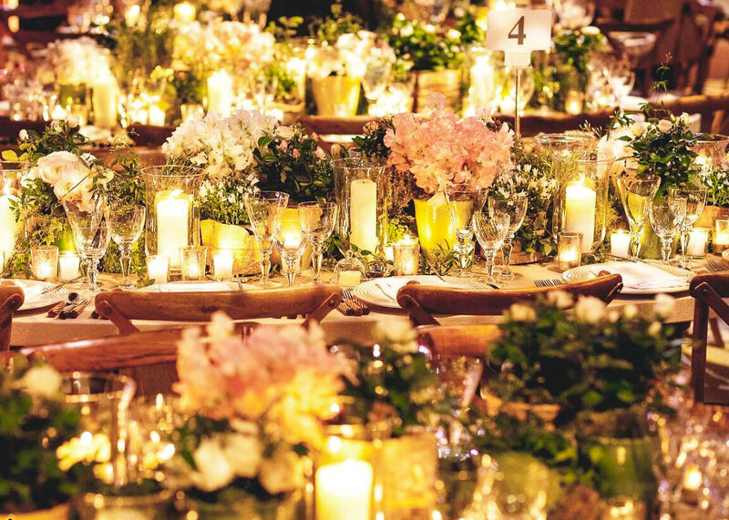 A wedding reception glows with candlelight amongst pots of flowers at a luxury wedding or party.