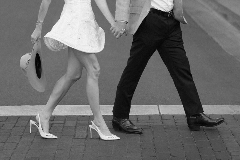 A black and white portrait of a couple along the rocky shoreline as waves crash behind them — a serene, romantic engagement session captured by Kelly Lugo Photo.