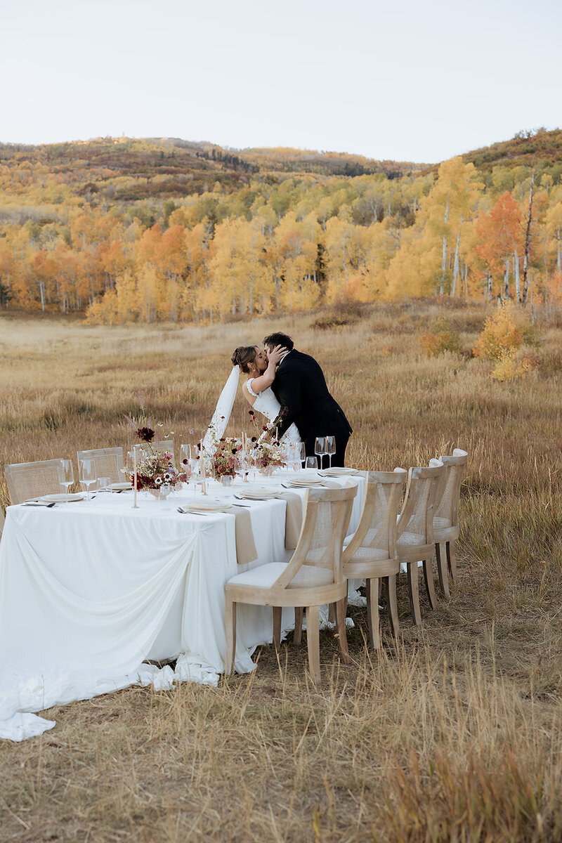 Couple sharing kiss at their elopement with reception table decorated.