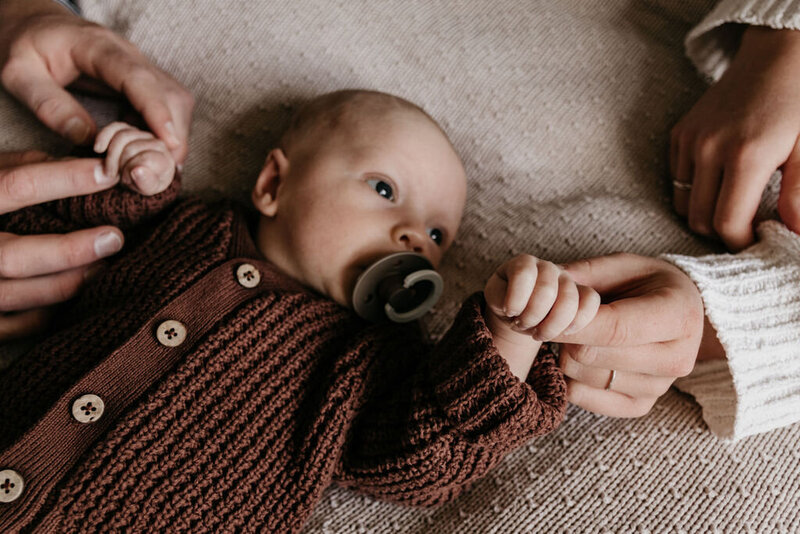 Newbornbaby tijdens een newbornshoot met de handjes in de handen van zijn ouders