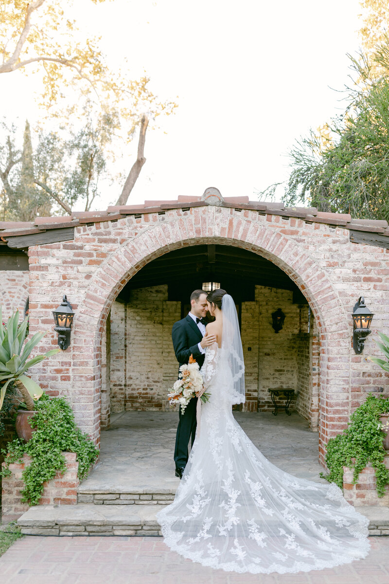 Bride and groom embrace in front of brick archway on their wedding day