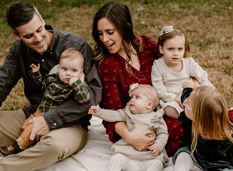 Mom and dad sitting on a blanket holding their twins and sitting with their older daughters wearing fall colors in Annapolis Maryland.