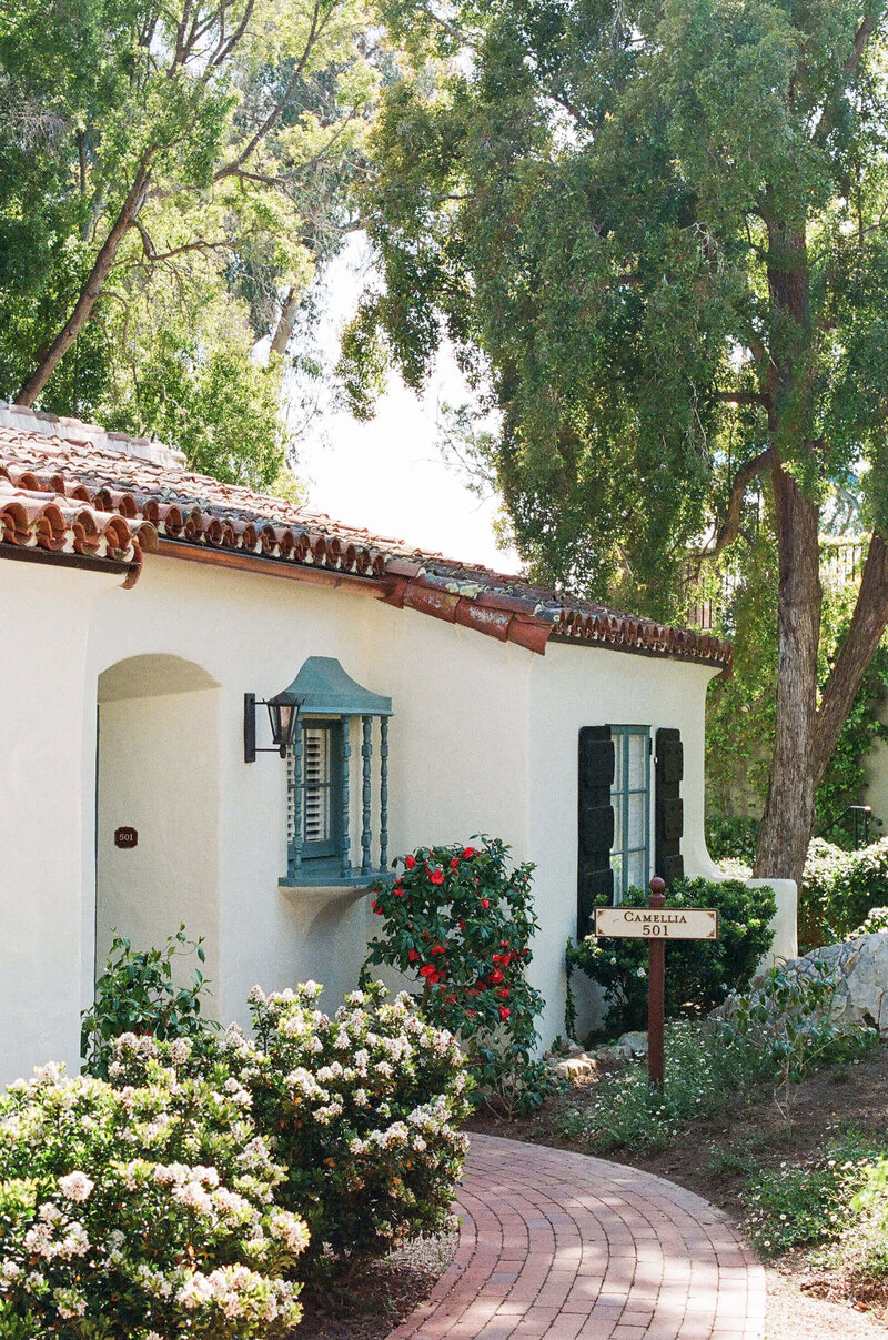 An exterior view of a charming Santa Barbara wedding location with large flowering bushes and a brick path, marked with a sign that reads, “Camellia 501”