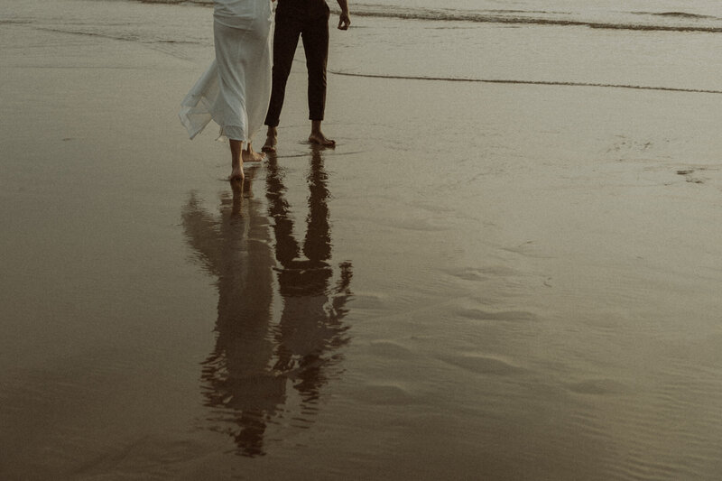 A couple's shoot on the Oregon coast. Detail shot of them walking along the beach with their silhouettes reflecting on the wet sand.