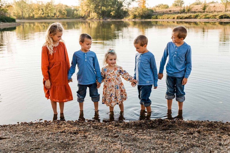 Group of brothers and sisters hold hands and smile at each other while wading in a lake