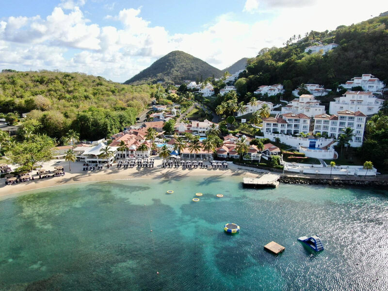 A stunning aerial view of a beachfront resort with turquoise waters and lush greenery, perfect for destination weddings and honeymoon planning.