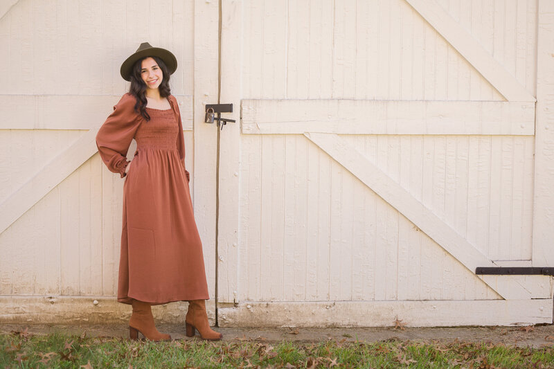 A teenage girl wearing a flowing orange autumn dress posing confidently during a Valley Forge mini session, with golden leaves in the backdrop.